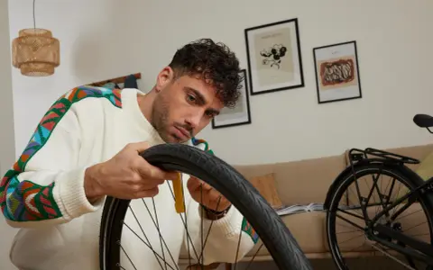 Mężczyzna w kolorowym swetrze naprawia rower, wyjmując dętkę.