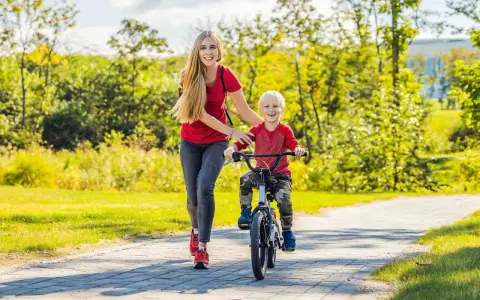 Mama uczy synka, jak nauczyć dziecko jeździć na rowerze. Radosny chłopiec pedałuje, a mama go asekuruje.