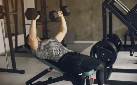 Mężczyzna wykonuje ćwiczenia na dol klatki piersiowej, podnosząc hantle na ławce skośnej.