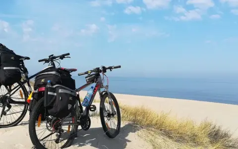 Dwa rowery z sakwami na plaży, gotowe na przygodę wzdłuż Velo Baltica. Morze i niebo tworzą tło.