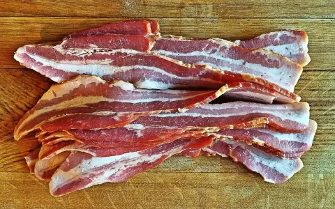 Surowy boczek ułożony na drewnianej desce. Idealny do chrupiącego smażenia, ale pamiętaj o jego kaloryczności - boczek kcal.