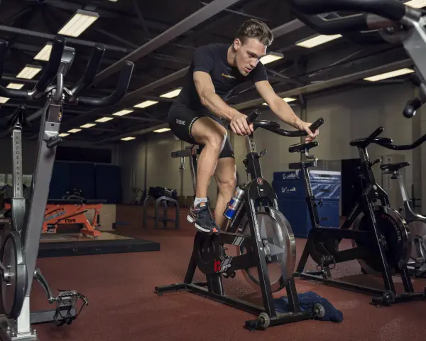 Mężczyzna intensywnie pedałuje na rowerze stacjonarnym, wykonując trening anaerobowy.