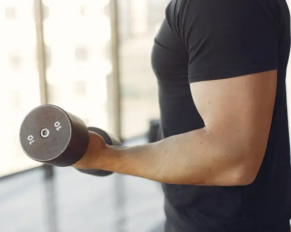 Mężczyzna w czarnej koszulce wykonuje ćwiczenia na biceps z hantlem 10 kg. To jedne z najlepszych ćwiczeń na biceps.