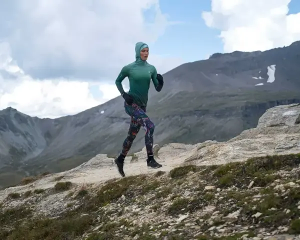 Kobieta w sportowym hidżabie biegnie po górskim szlaku, doskonaląc swoją kadencję w bieganiu.