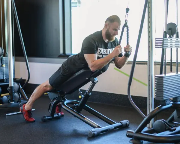 Mężczyzna wykonuje ćwiczenie na triceps, znane jako skull crushers, na ławce skośnej z użyciem wyciągu.