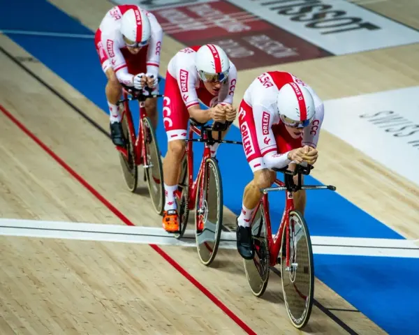Trzech kolarzy w biało-czerwonych strojach ściga się na welodromie. Ich rowery i stroje mają logo ORLEN. To dynamiczne keirin kolarstwo.