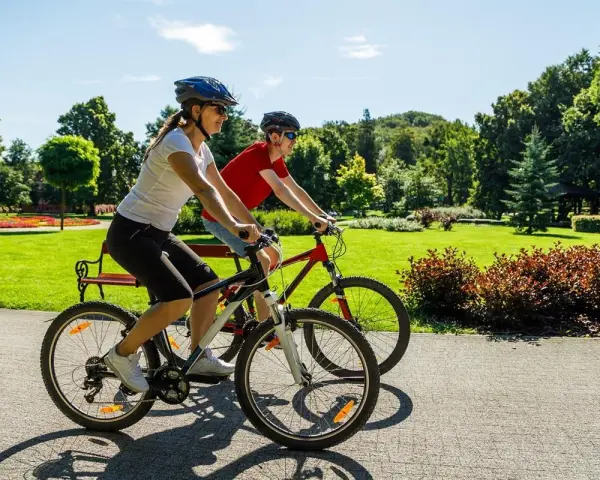 Dwie osoby na rowerach cieszą się pięknym dniem w parku. To pokazuje, co daje jazda na rowerze: radość, aktywność i kontakt z naturą.