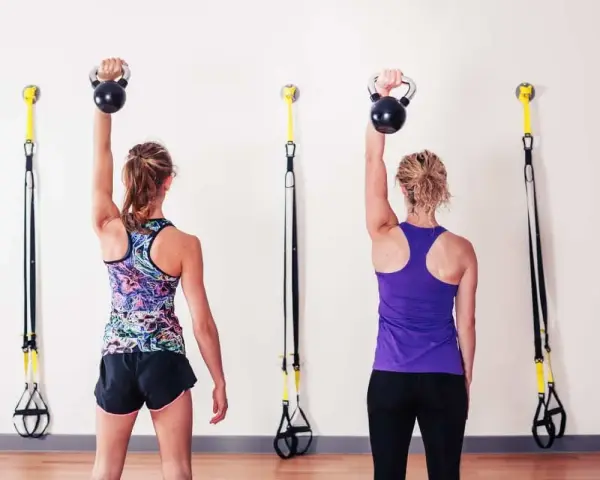 Dwie kobiety wykonują ćwiczenia z kettlebell, aby wzmocnić mięśnie i zapobiec bólowi barku.