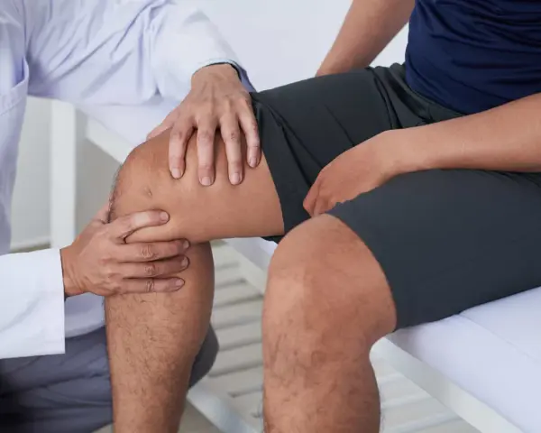 Fizjoterapeuta bada kolano pacjenta, sugerując ćwiczenia na chondromalację rzepki.