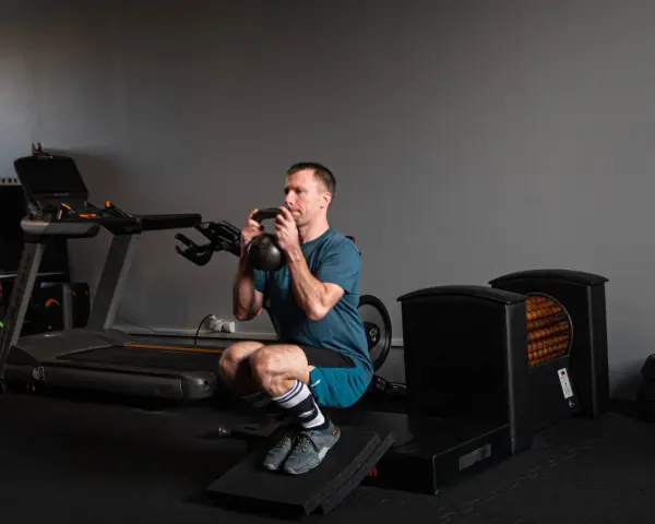 Mężczyzna wykonuje głęboki **squat** z kettlebell w rękach, ćwicząc siłę w siłowni.