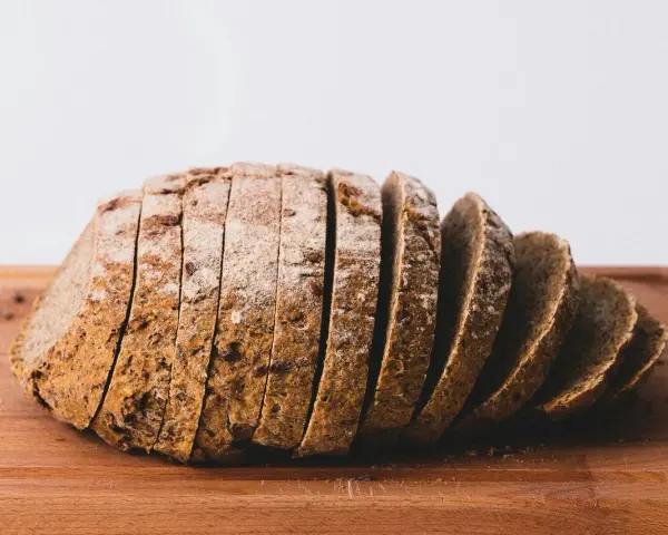 Pokrojony bochenek chleba żytniego na drewnianej desce. Zastanawiasz się, ile kcal ma kromka chleba?