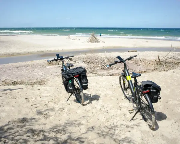 Dwa rowery z sakwami na piaszczystej plaży, gotowe do odkrywania tras rowerowych nad morzem.