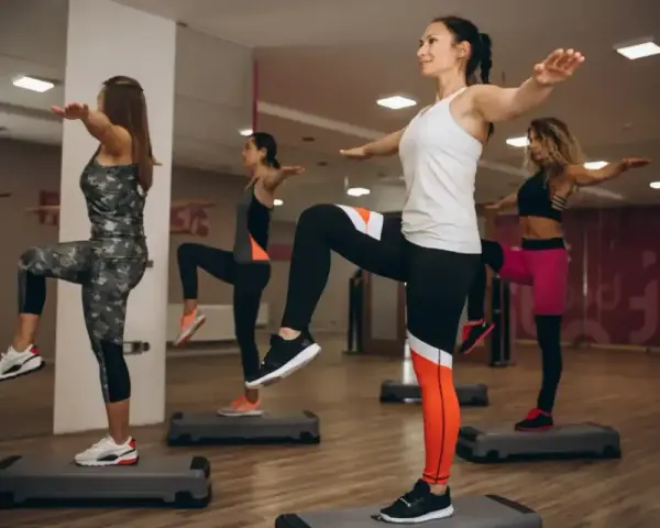 Kobiety ćwiczą aerobik na stepach, podnosząc kolana i wyciągając ręce.