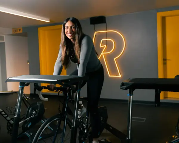 Uśmiechnięta kobieta na rowerze stacjonarnym, gotowa na intensywny trening cardio.