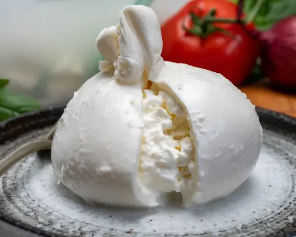 Pyszna burrata na talerzu, z pomidorem i cebulą w tle. Zastanawiasz się nad burrata kcal?