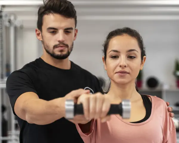 Trening dla początkujących: mężczyzna pomaga kobiecie podnosić hantle.