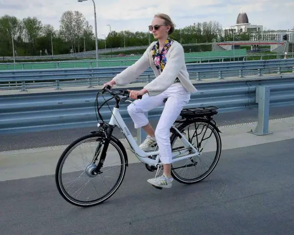 Kobieta w białych spodniach i sweterku jedzie na rowerze elektrycznym. Przepisy dotyczące rowerów elektrycznych są ważne dla bezpieczeństwa.