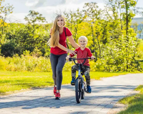 Mama uczy synka, jak nauczyć dziecko jeździć na rowerze. Radosny chłopiec pedałuje, a mama go asekuruje.