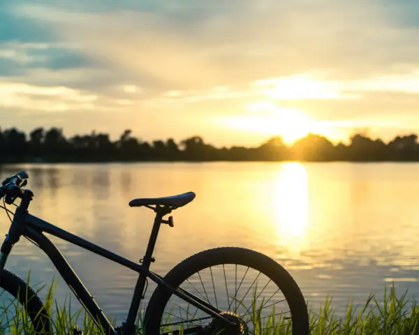 Rower na tle zachodzącego słońca nad jeziorem. Idealne miejsce na odkrywanie tras rowerowych Mazur.