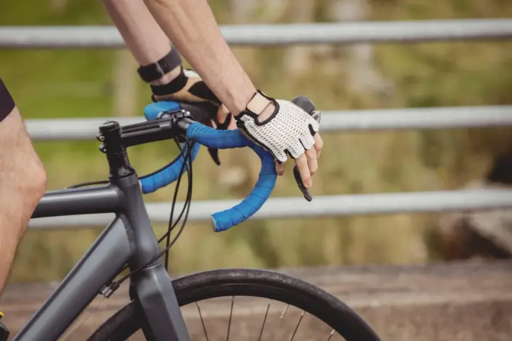 Rowerzysta w rękawiczkach trzyma kierownicę, zbliżając się do swojego progu mleczanowego.