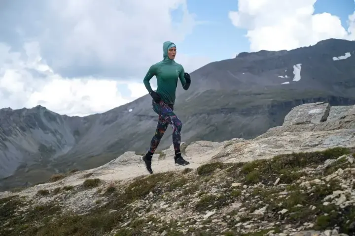 Kobieta w sportowym hidżabie biegnie po górskim szlaku, doskonaląc swoją kadencję w bieganiu.