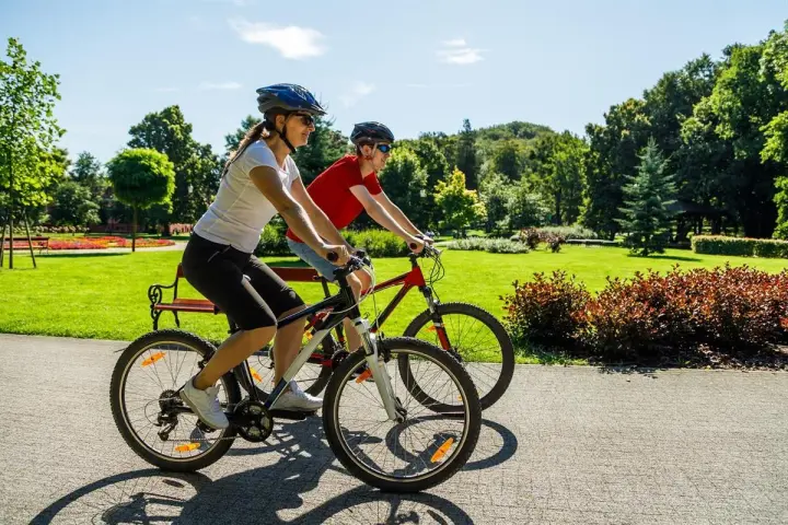 Dwie osoby na rowerach cieszą się pięknym dniem w parku. To pokazuje, co daje jazda na rowerze: radość, aktywność i kontakt z naturą.