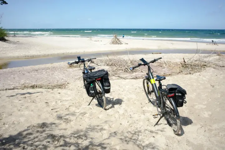 Dwa rowery z sakwami na piaszczystej plaży, gotowe do odkrywania tras rowerowych nad morzem.