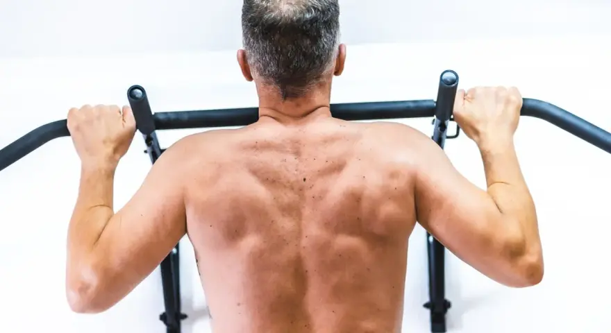 Mężczyzna wykonuje ćwiczenia na plecy, podciągając się na drążku.