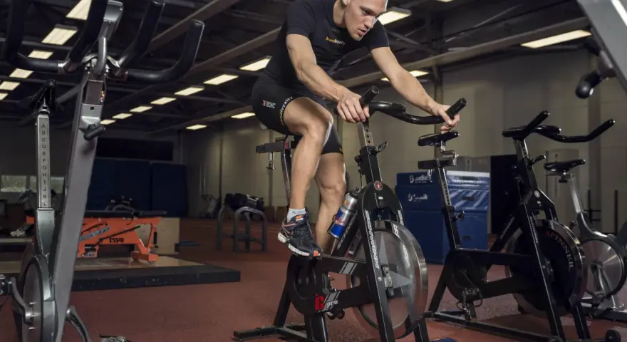 Mężczyzna intensywnie pedałuje na rowerze stacjonarnym, wykonując trening anaerobowy.