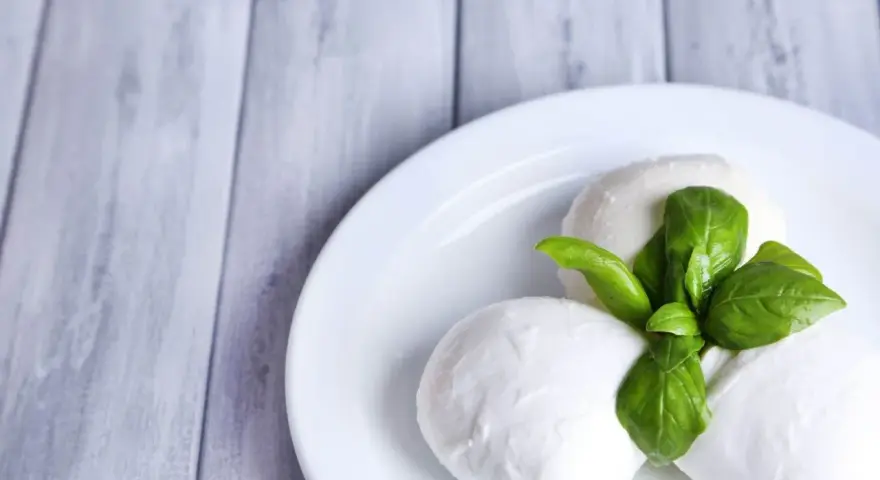 Trzy kulki serka mozzarella z listkami bazylii na białym talerzu. Idealne do sałatki, znasz ser mozzarella kcal?