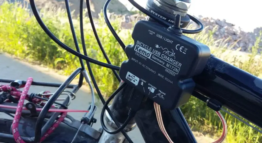 Ładowarka rowerowa Kemo zasilana przez **dynamo**, podłączona do kierownicy, z kablem USB.
