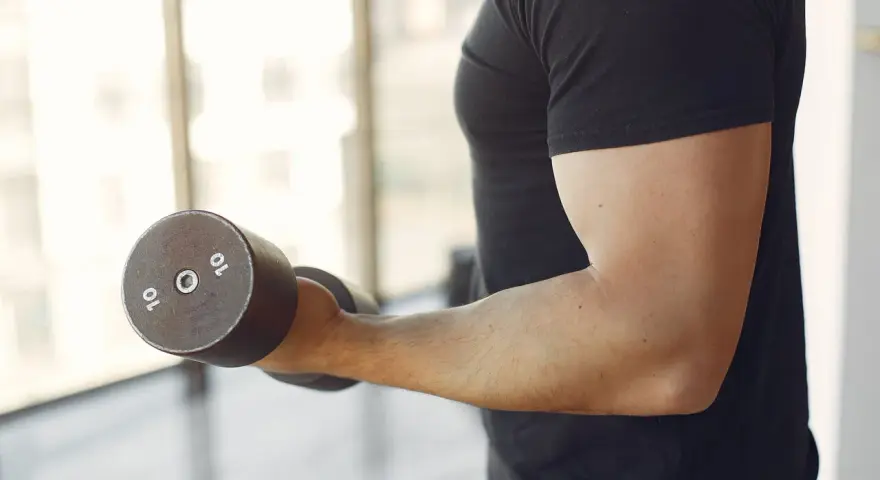 Mężczyzna w czarnej koszulce wykonuje ćwiczenia na biceps z hantlem 10 kg. To jedne z najlepszych ćwiczeń na biceps.