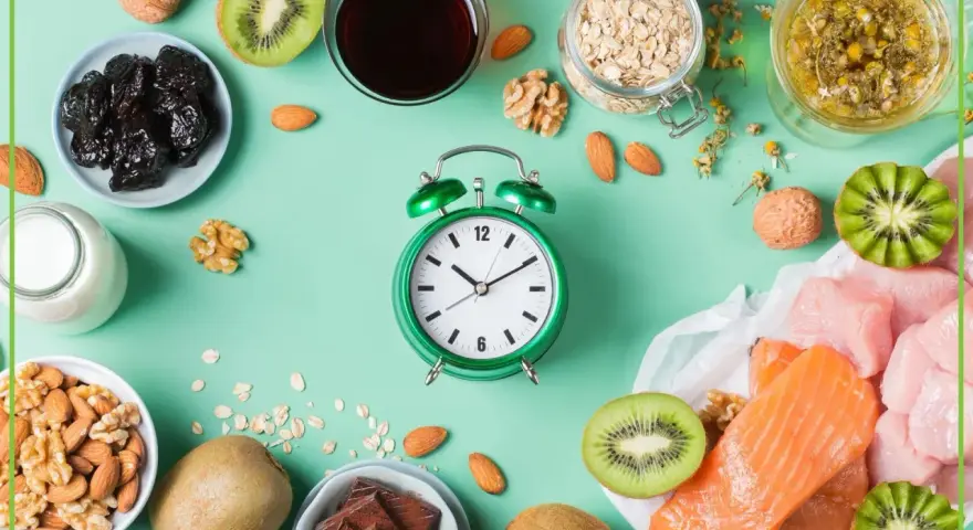 Zielony budzik obok produktów bogatych w tryptofan: łososia, indyka, kiwi, orzechów, migdałów, śliwek, mleka, owsa i czekolady. Zastanawiasz się, po jakim czasie działa tryptofan?