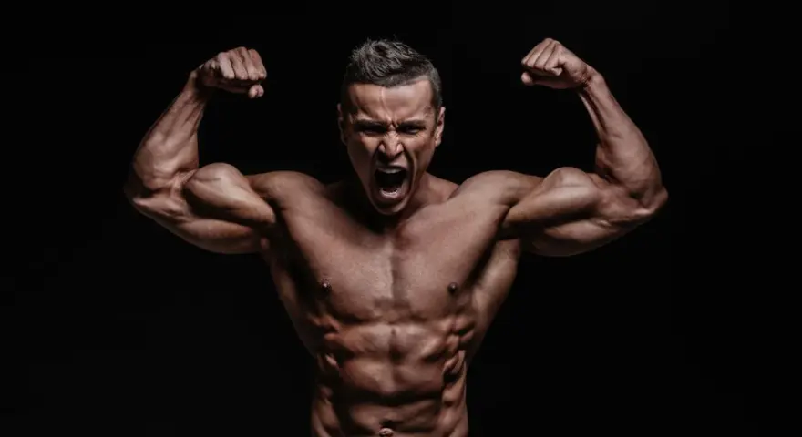 Mężczyzna z wyrzeźbionymi mięśniami napina bicepsy, krzycząc z wysiłku. Jego sylwetka sugeruje intensywny trening, być może z użyciem clenbuterolu.