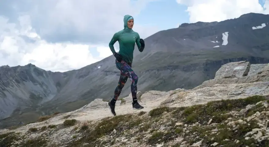 Kobieta w sportowym hidżabie biegnie po górskim szlaku, doskonaląc swoją kadencję w bieganiu.
