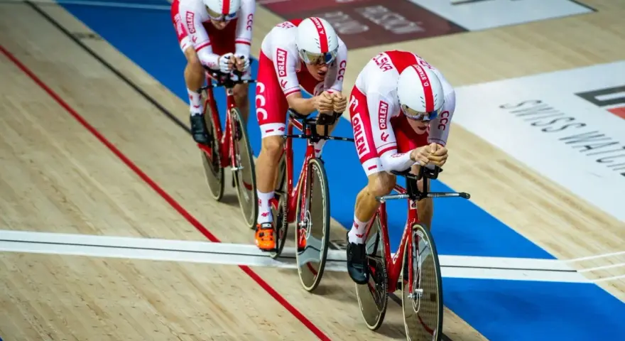 Trzech kolarzy w biało-czerwonych strojach ściga się na welodromie. Ich rowery i stroje mają logo ORLEN. To dynamiczne keirin kolarstwo.