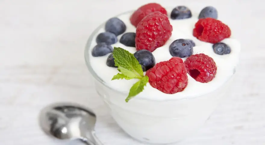 Pyszny jogurt z malinami i borówkami, idealny na śniadanie lub jako element diety jogurtowej. Obok leży łyżeczka.