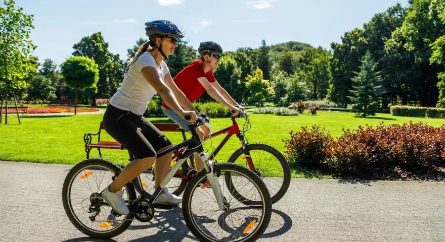 Dwie osoby na rowerach cieszą się pięknym dniem w parku. To pokazuje, co daje jazda na rowerze: radość, aktywność i kontakt z naturą.