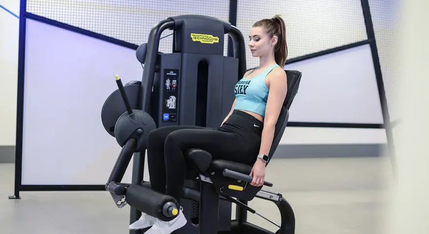 Kobieta wykonuje wyprosty nóg na maszynie Technogym, ćwicząc mięśnie czworogłowe uda.