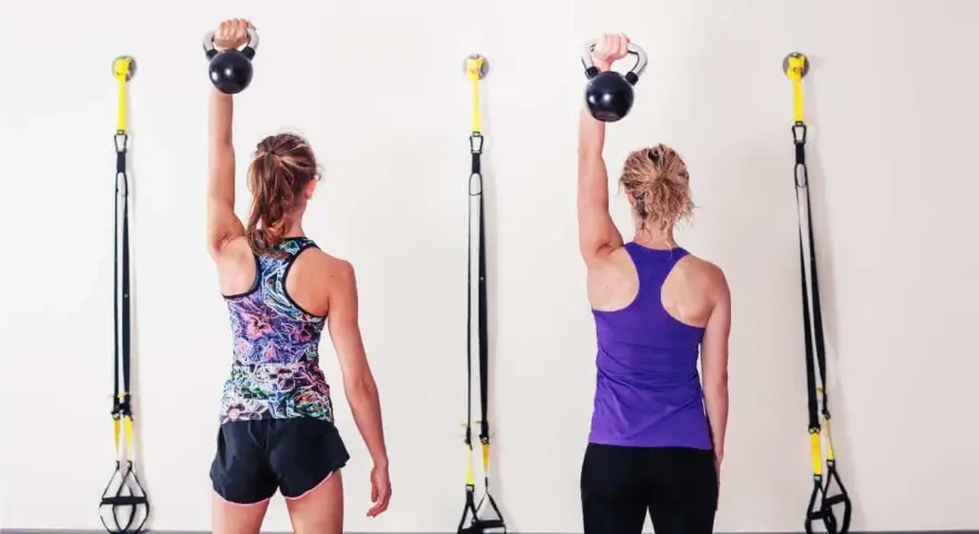Dwie kobiety wykonują ćwiczenia z kettlebell, aby wzmocnić mięśnie i zapobiec bólowi barku.