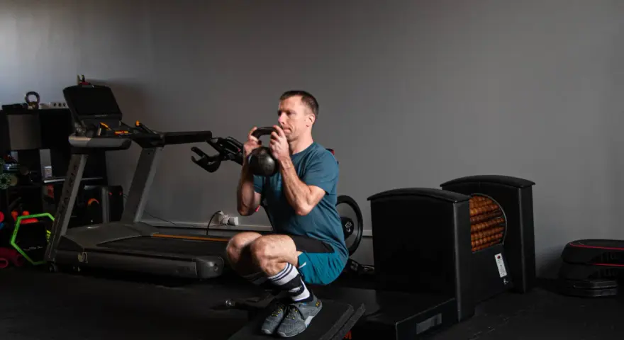 Mężczyzna wykonuje głęboki **squat** z kettlebell w rękach, ćwicząc siłę w siłowni.