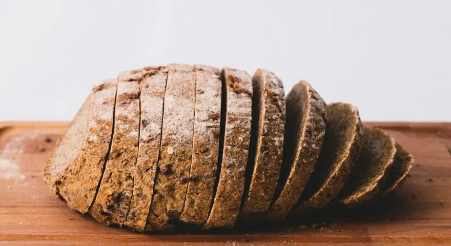 Pokrojony bochenek chleba żytniego na drewnianej desce. Zastanawiasz się, ile kcal ma kromka chleba?