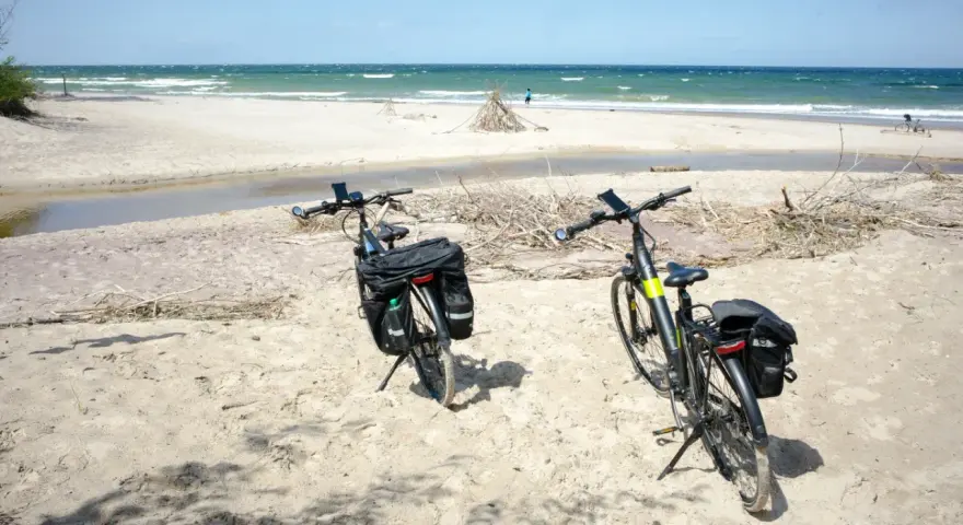 Dwa rowery z sakwami na piaszczystej plaży, gotowe do odkrywania tras rowerowych nad morzem.