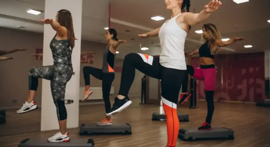 Kobiety ćwiczą aerobik na stepach, podnosząc kolana i wyciągając ręce.