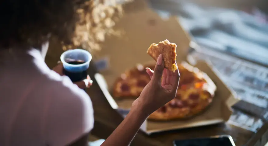 Kobieta trzyma kawałek pizzy i napój, czując głód. Grelina działa, apetyt rośnie.