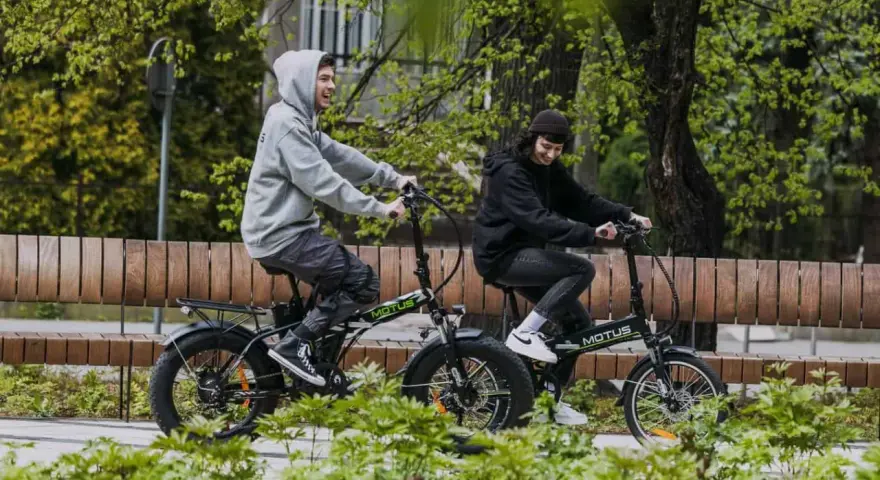 Dwaj młodzi ludzie cieszą się jazdą na rowerach elektrycznych. Dofinansowanie do roweru elektrycznego sprawia, że ekologiczny transport jest dostępny dla każdego.