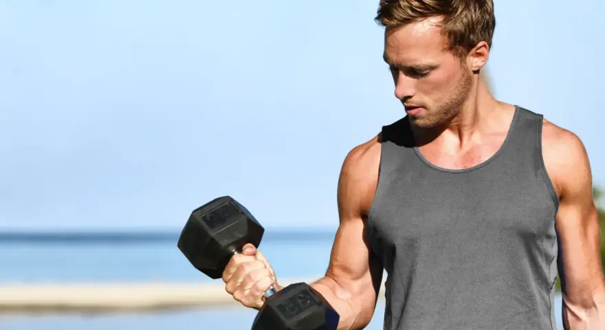 Mężczyzna ćwiczy biceps z hantlem. Zastanawia się, ile serii na klatę w tygodniu będzie optymalne dla jego treningu.