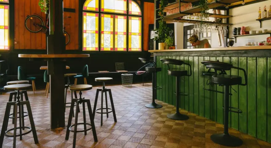 Wnętrze kawiarni z zielonym barem, stołkami i rowerem na ścianie. Idealne miejsce na coffee ride.
