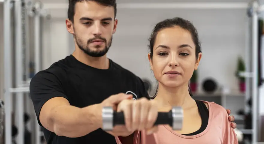 Trening dla początkujących: mężczyzna pomaga kobiecie podnosić hantle.