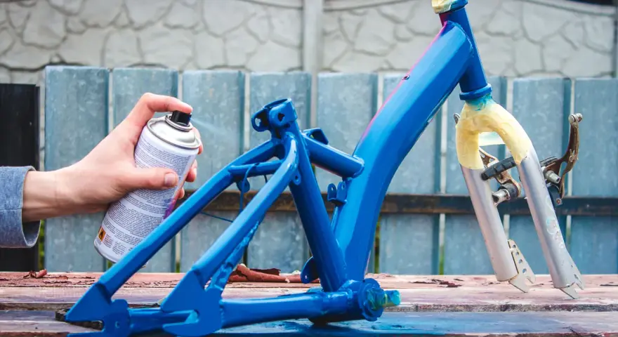 Ręka trzymająca puszkę z farbą w sprayu, malująca niebieską ramę roweru.